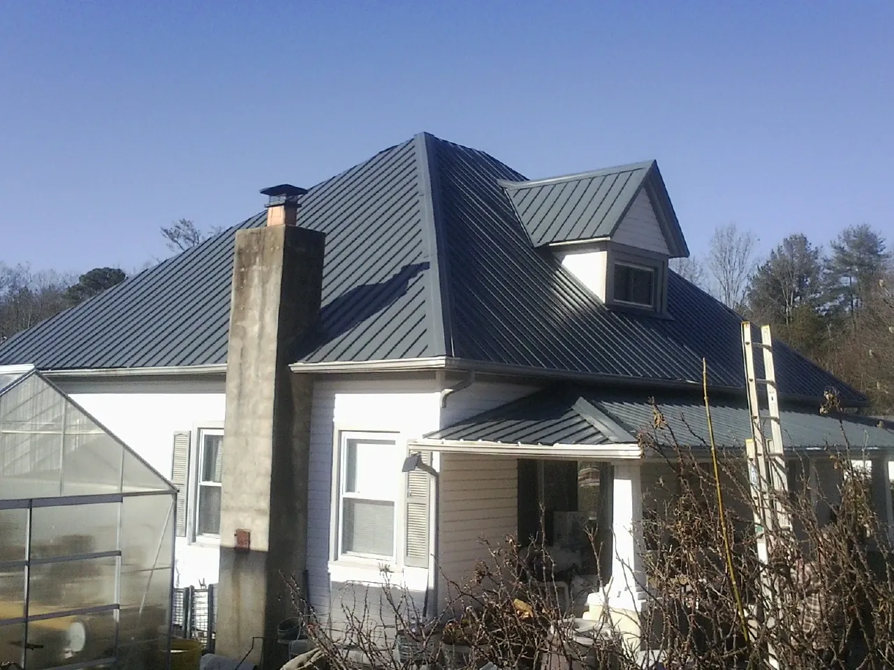Dark blue standing seam metal roof on a white farmhouse with dormer — Slate & Tile Roof Repair by Roofing Brothers in Christiana