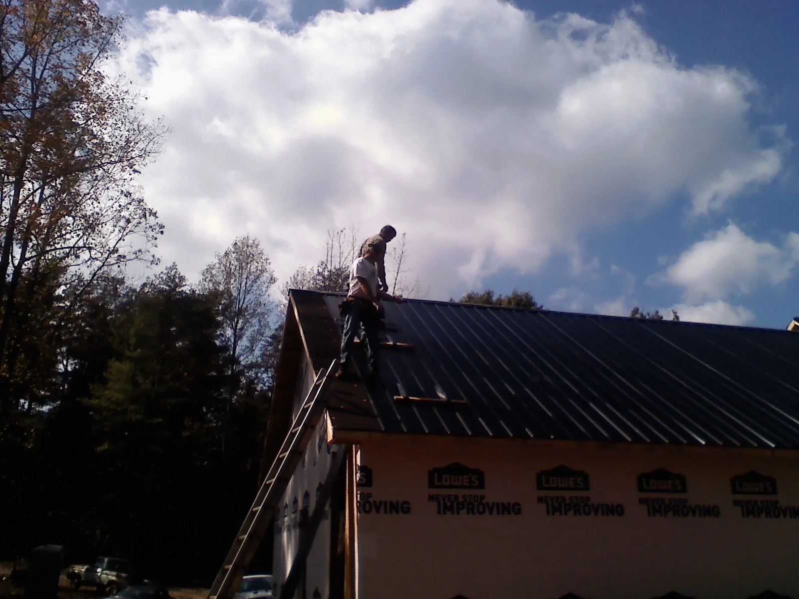 Roofer fastening dark metal panels high against a cloudy sky, from a Roof Inspection job in Christiana