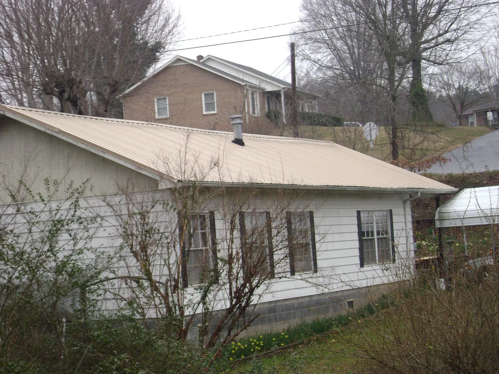 Tan metal roof on a white sided house set into a hillside — Commercial Roofing by Roofing Brothers in Christiana